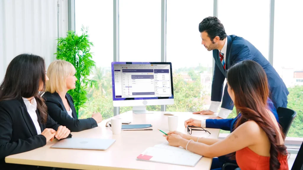 Data center operations team reviewing Ubersmith billing platform on desktop monitor during a collaborative office meeting AI colocation billing software Florida.