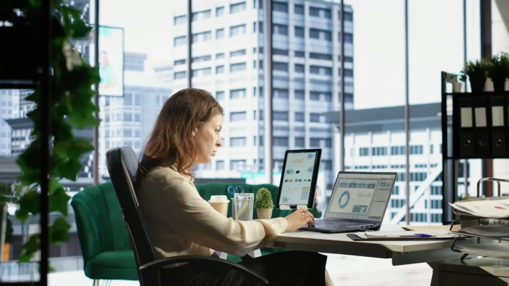 A professional working at a desk analyzing data and dashboards on multiple screens in a modern office with a cityscape view, representing operational oversight and data-driven decision-making, AI Billing Automation for New York ISPs.
