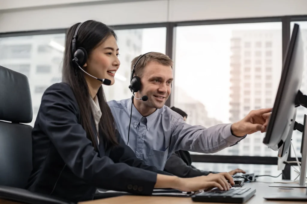 Two telecom professionals wearing headsets reviewing data on a monitor in a modern office environment, automated telecom billing system in USA.